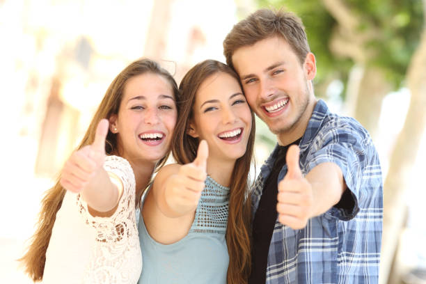 three happy friends smiling with thumbs up in the street - aluno dentista imagens e fotografias de stock