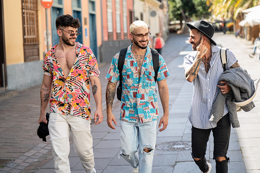 Three happy young men walking in the city, talking to each other, having fun. Multiethnic group of friends. Real people lifestyle.