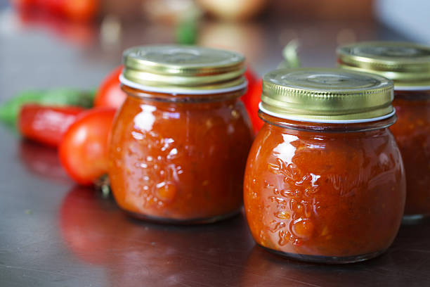 Three jars of tomato chutney on a table with the tomatoes stock photo
