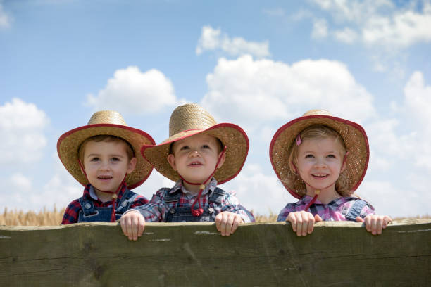 three little cowboys outdoors in a field stock photo