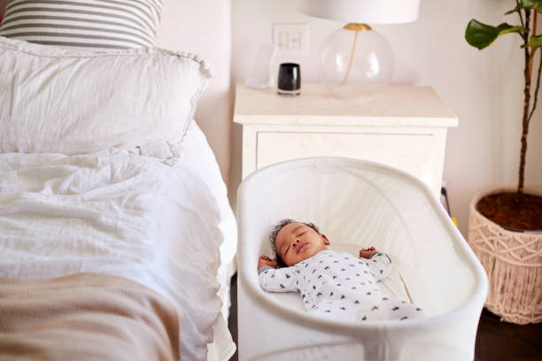 Drie maanden oude baby in slaap in zijn bedje naast het bed in zijn motherâ "u20acs slaapkamer​​​ foto