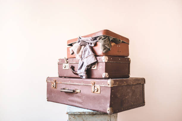 Three old vintage suitcases with clothes on a light wall background. Rustic Retro Style stock photo