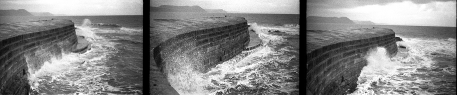 35mm black and white photos of a wave rolling up against the sea wall, the cobb, in Lyme Regis, Dorset.