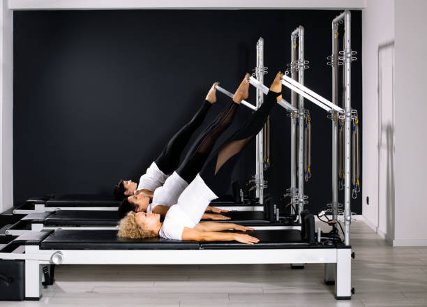 Three Pilates women in reformer tower exercise at gym stock photo