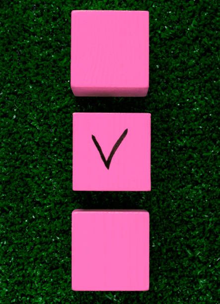 Three pink cubes with a tick on one on grass Three pink cubes with a tick on one on grass. Concept of choosing a better option, creating checklists, elections and sports betting football betting analytics stock pictures, royalty-free photos & images