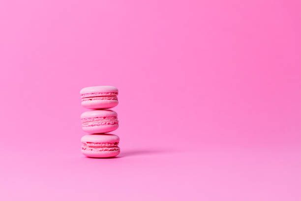Three pink macaroons with pink filling stacked on pink background stock photo