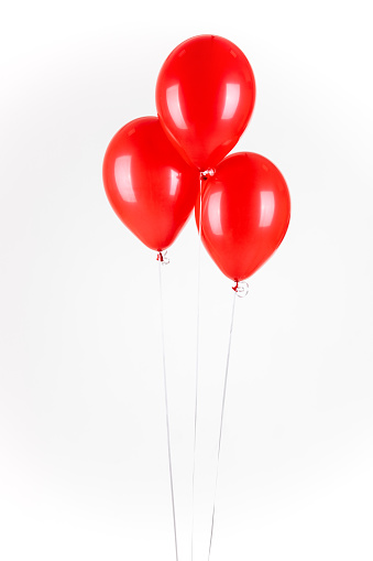 Three bright red balloons flying in front of plane white background. The are on different height and are shiny and simple.