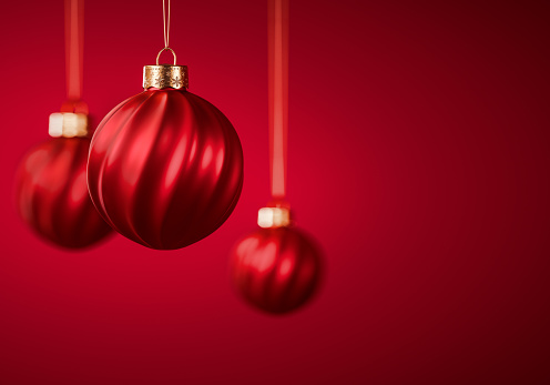 Three red Christmas balls. Twisted striped Christmas ornaments hanging against burgundy red background. Christmas decoration, festive atmosphere concept. Selective focus, copy space.