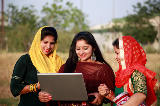 Three rural women using laptop together outdoors in field stock photo