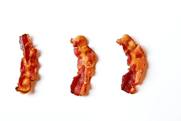 Three Slices of Bacon Isolated on a White Background Three slices of fresh fried bacon lined up in a row isolated on a white background bacon stock pictures, royalty-free photos & images