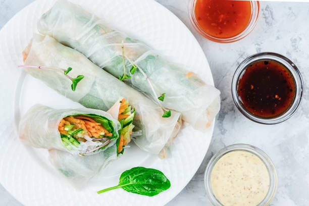 Three spring rolls lie on a white plate; one of them is cut in half. A healthy Asian snack with vegetables in rice paper. stock photo