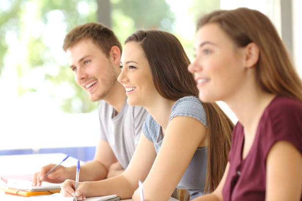 Three students listening in a classroom Side view of three happy attentive students listening to a class in a classroom college students in classroom stock pictures, royalty-free photos & images