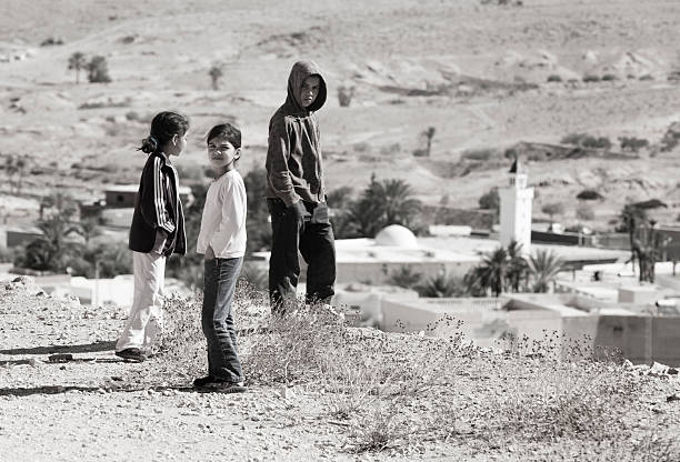 Three Tunisian children over a village Deuz, Tunisia, March 30, 2013: Three children, two girls wearing trousers and jackets and a boy with a hooded jacket, are standing high over a small village tunisian girls stock pictures, royalty-free photos & images