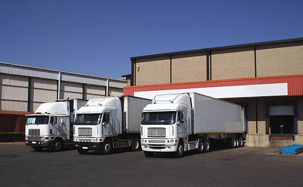 Three white freight trucks at a warehouse loading dock stock photo