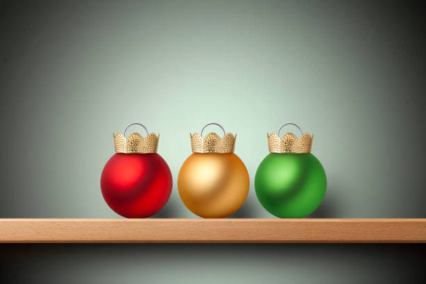 Three colored Christmas balls with the top upside down similar to a royal crown on shelf.