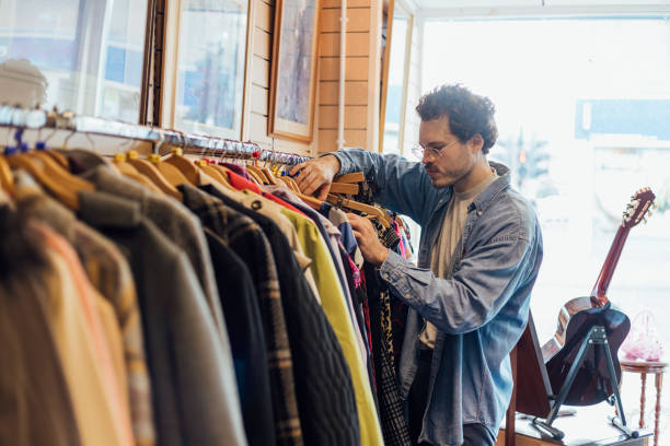 Thrift Store Shopping Man looking through clothing while at a thrift store. flea market photos stock pictures, royalty-free photos & images