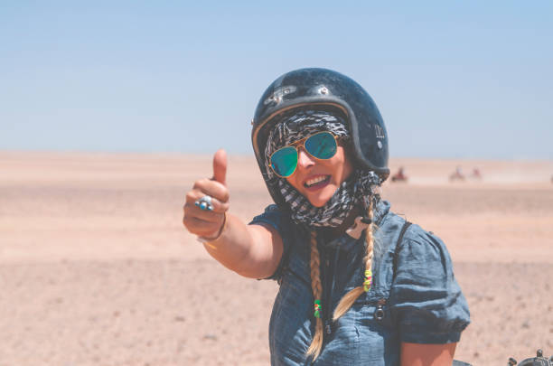 Thumbs up for this ride Atrractive Woman on Safari ride in desert showing thumbs up.Beautiful young Woman with safety helmet driving  bike.Female tourist in Sahara adventure.Copy space hot egyptian women stock pictures, royalty-free photos & images