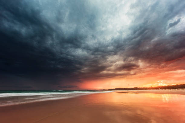Tidal retreat reflecting dramatic storm on the beach at sunset stock photo
