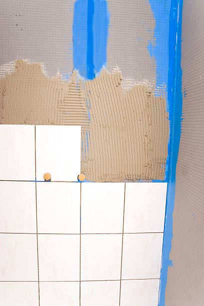 Tile Work "Home improvement background, tile work at a new batroom shower. A special reinforced polymer foam board with modified cement face is used to protect the walls against moisture. Tiles installed around the water connections, blue sealing compound between two foam boards and the corner. Partially tile adhesive applied to the boards, selective focus." foamcore stock pictures, royalty-free photos & images