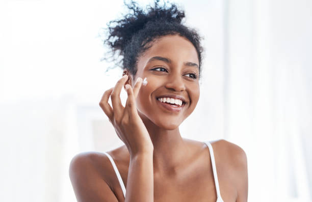 Time for a fresh start Shot of a beautiful young woman applying moisturiser to her face in the bathroom at home applying stock pictures, royalty-free photos & images