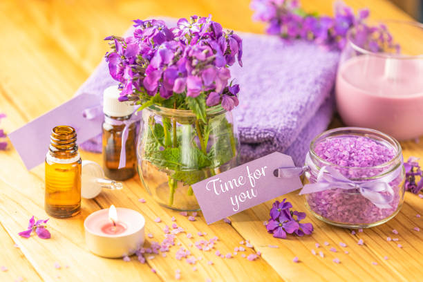 Time for you text phrase on label sticker. Spa still life with violet oil, towel, violaceous bath salt in glass jar and perfumed candle on natural wood table surface stock photo