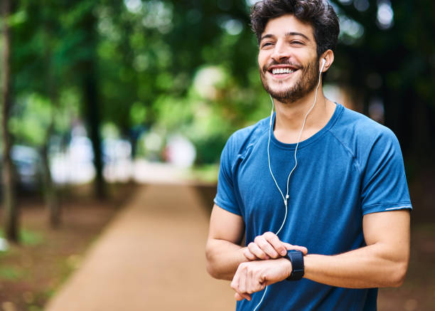 Time to clock another personal best Shot of a sporty young man checking his watch while exercising outdoors headphones photos stock pictures, royalty-free photos & images