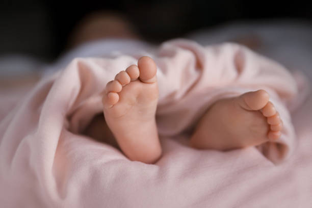 Tiny baby girl feet covered with soft pastel peach blanket, adorable small toes stock photo