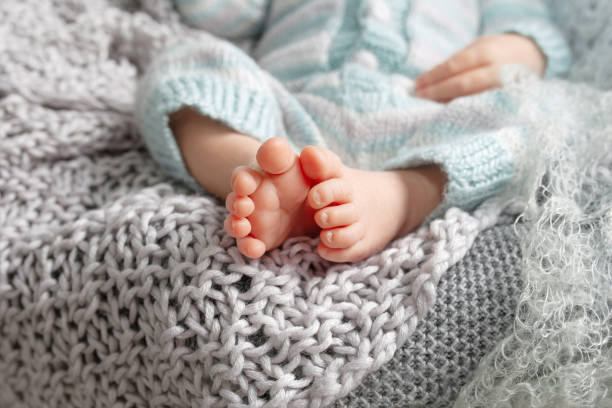 Tiny foot of newborn baby. Soft newborn baby feet against a beige  blanket. Baby feet with toes curled up stock photo