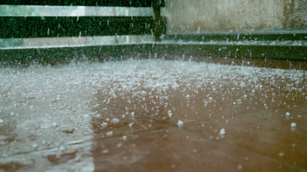 CLOSE UP: Tiny grains of soft hail fall on the wet brown floor of a balcony stock photo