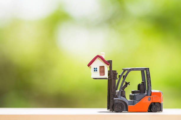 tiny home with miniature toy forklift machine, over blurred green spring garden background. stock photo
