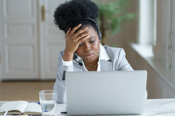 Tired african female support call center worker in headset frustrated look upset on laptop screen stock photo