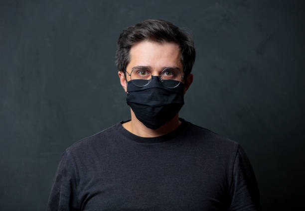 Tired brunet man in in black facemask on dark background stock photo