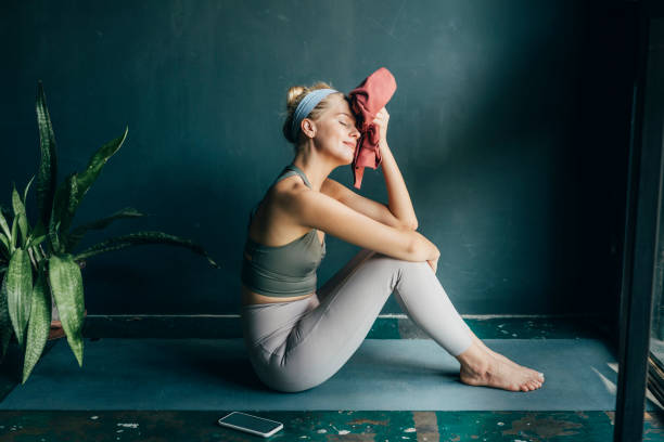 müde, aber glücklich: fit blonde frau wisch ihr gesicht mit einem handtuch nach einem home workout - yoga fotos stock-fotos und bilder