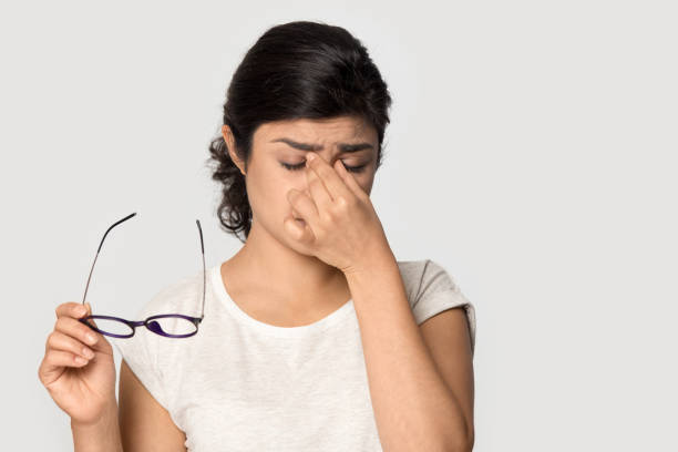 Tired Indian girl taking off glasses, feeling eye strain Tired Indian girl taking off glasses, massing nose bridge isolated on grey studio background, exhausted young woman feeling eye strain, unhappy stressed student, teacher feeling unwell eye care  stock pictures, royalty-free photos & images