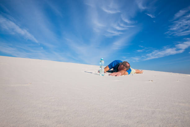 Tired man lies in the sand next to a bottle of water stock photo