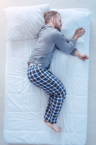 Tired millennial man falling asleep after working hard Recharging my batteries. Top view on a young man wearing pajamas taking a nap and sleeping tight after getting tired at home. man sleeping in bed top view stock pictures, royalty-free photos & images