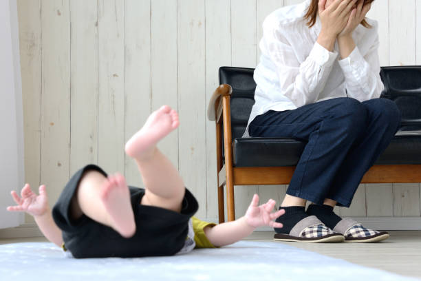 居間で疲れた母親と泣いている赤ちゃん - 子供　不機嫌 ストックフォトと画像