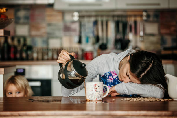 madre stanca, che cerca di versare caffè al mattino. donna sdraiata sul tavolo della cucina dopo una notte insonne - esaurimento foto e immagini stock
