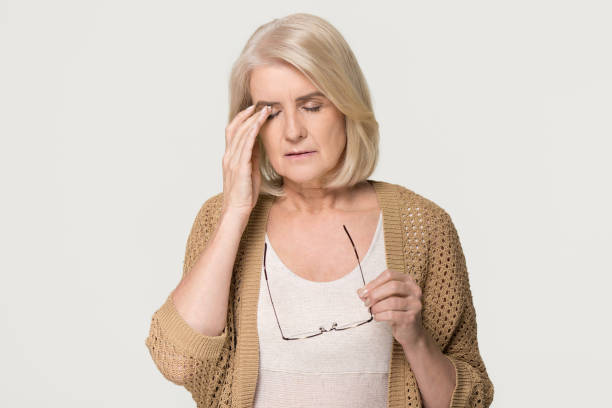 Tired old woman holding glasses feeling eyestrain isolated on background Upset tired old mature woman taking off glasses feeling eyestrain pain, stressed aged senior lady suffer from headache bad vision eye strain fatigue problem isolated on grey white studio background lid stock pictures, royalty-free photos & images