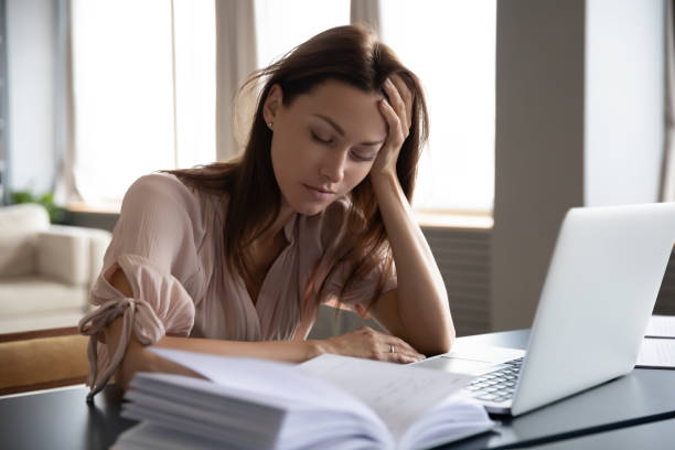 donna stanca e assonna seduta alla scrivania con il laptop, che tiene la testa - esaurimento foto e immagini stock