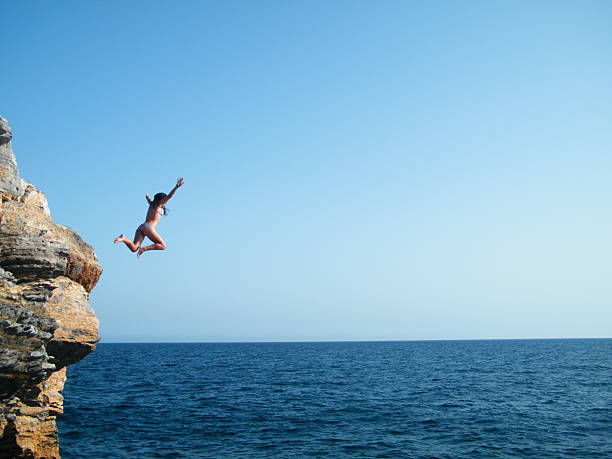 To give the jump Cartagena, Murcia, Spain - August, 16, 2012: "El portús" beach. A group of young  they amuse jumping. The photo is made when one of the girls jumps into the sea from the rocks cliff jumping stock pictures, royalty-free photos & images