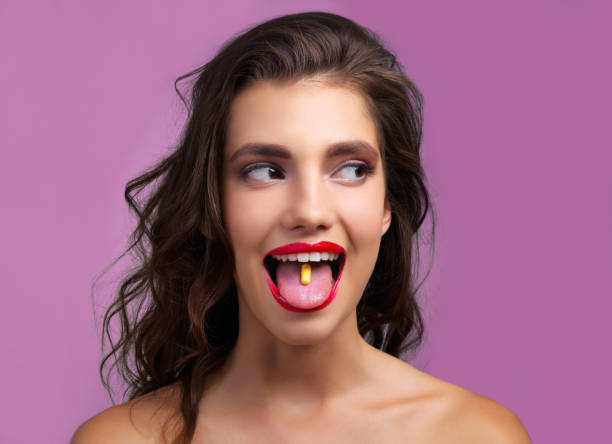To medicate or not to medicate? Studio shot of a beautiful young woman with a pill in her mouth against a purple background healthy tongue stock pictures, royalty-free photos & images