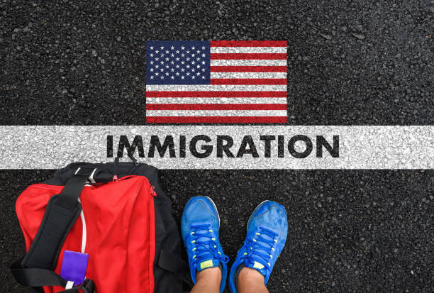 IMMIGRATION to United States Man in shoes with bag standing next to line with word IMMIGRATION and flag of the United States on asphalt road emigration and immigration stock pictures, royalty-free photos & images