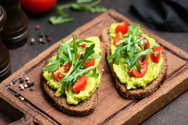Toast with mashed avocado, arugula Vegan or Vegetarian Toast with mashed avocado, arugula served on wooden board toasted bread photos stock pictures, royalty-free photos & images