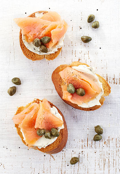 toasted bread with cream cheese and salmon fillet toasted bread with cream cheese and smoked salmon fillet on wooden table, top view caper stock pictures, royalty-free photos & images