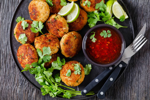 Tod man pla, thai fish cakes with lime, cilantro and sweet chili sauce on a black plate on a rustic wooden table, view from above, flat lay, macro stock photo