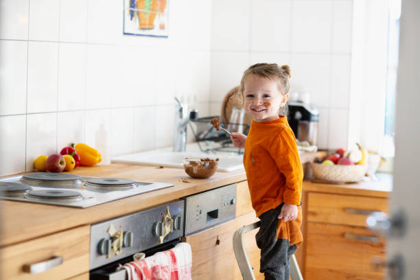 Toddler boy is eating chocolate mousse in kitchen stock photo