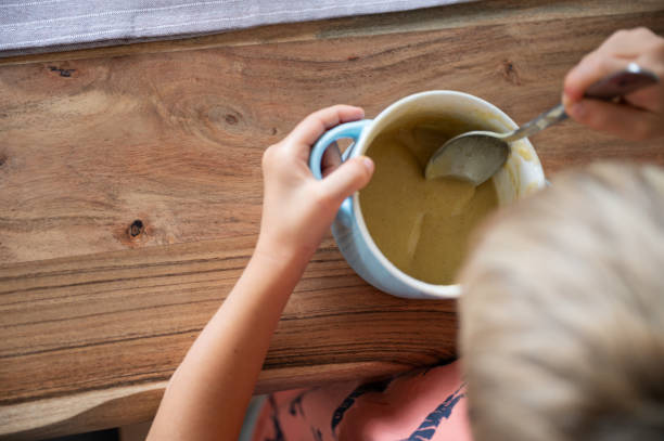 Toddler child eating creamed soup on wooden dinning table stock photo