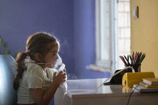 Close up photo of 3 years old girl sitting in living room and using nebulizer for allergy treatment. Shot indoor with a full frame mirrorless camera.