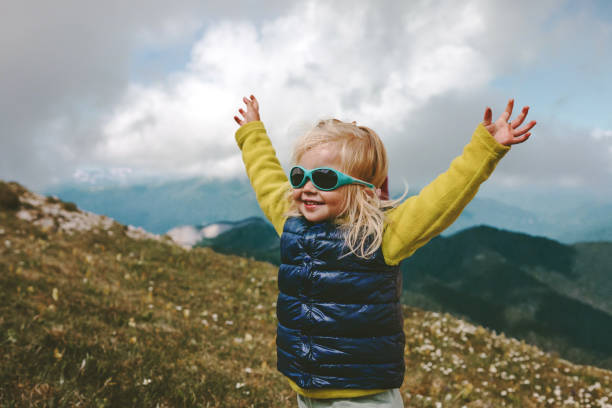 Toddler happy raised hands hiking in mountains family travel vacations healthy lifestyle 2 years old child outdoor having fun stock photo